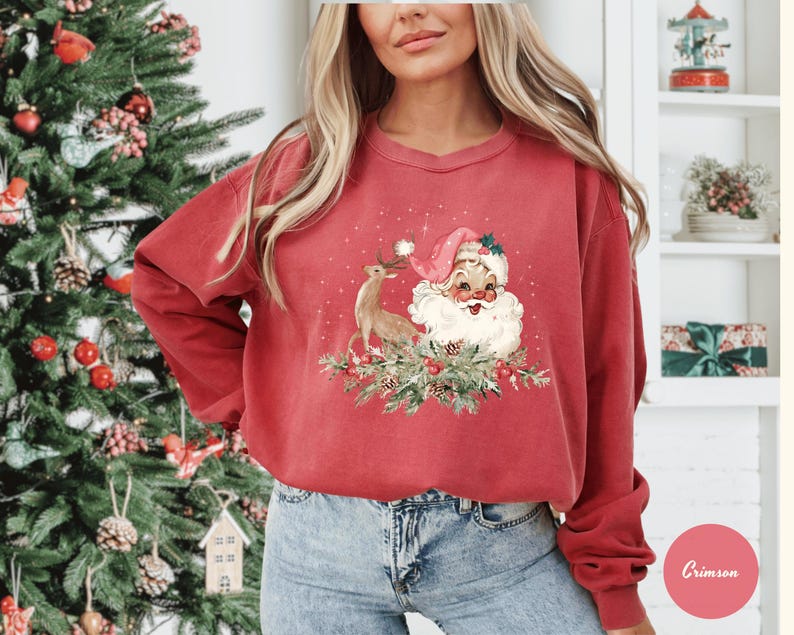 May include: A red sweatshirt featuring a vintage-style Christmas design. The graphic includes Santa Claus, a reindeer, and festive greenery. The sweatshirt has long sleeves and a crew neck.
