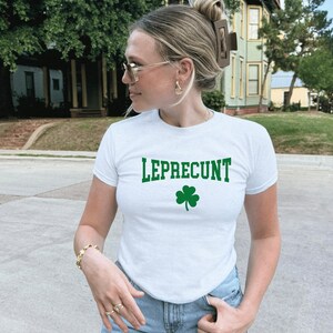 May include: White t-shirt featuring the word "LEPRECUNT" in green block letters and a green shamrock. The short-sleeved top has a crew neck.