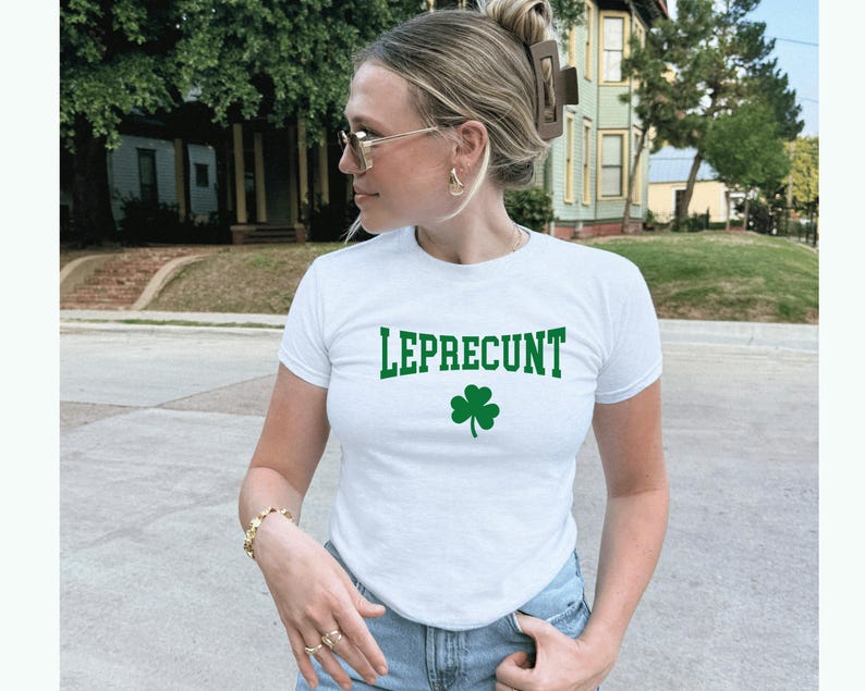 May include: White t-shirt featuring the word "LEPRECUNT" in green block letters and a green shamrock. The short-sleeved top has a crew neck.