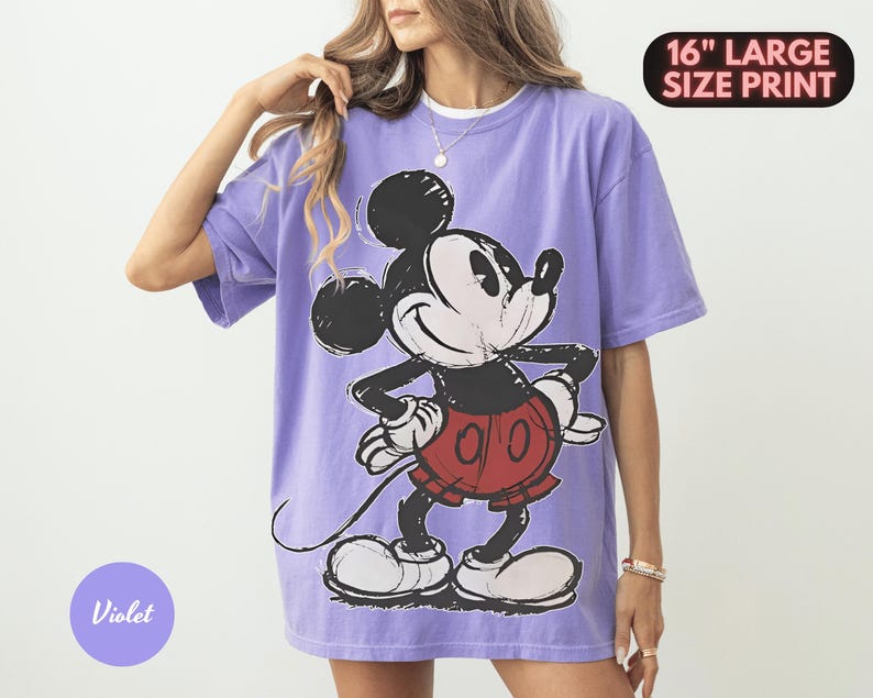 Puede incluir: Una camiseta violeta con un gran gr&aacute;fico de Mickey Mouse en negro, blanco y rojo. La camiseta tiene mangas cortas y un corte holgado. El texto en la camiseta dice "16" LARGE SIZE PRINT" y "Violet".