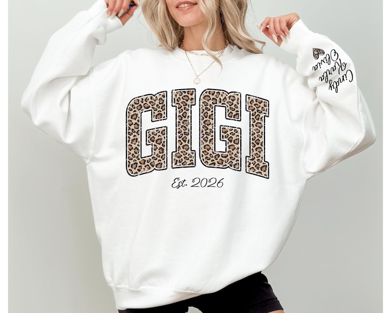 May include: A white sweatshirt with the word "GIGI" in a leopard print design. The text "Est. 2026" is below the word "GIGI". The sleeve has the names "Cindy Karla Olivia" printed on it.