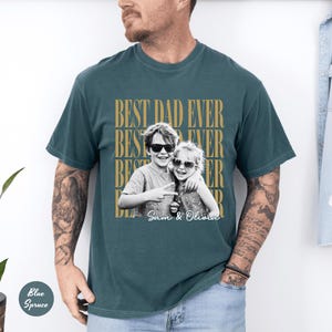 May include: Teal-colored t-shirt with the text "BEST DAD EVER" in a repeating pattern. A black and white photo of two children wearing sunglasses is centered on the shirt, with the names "Sam & Olivia" below.