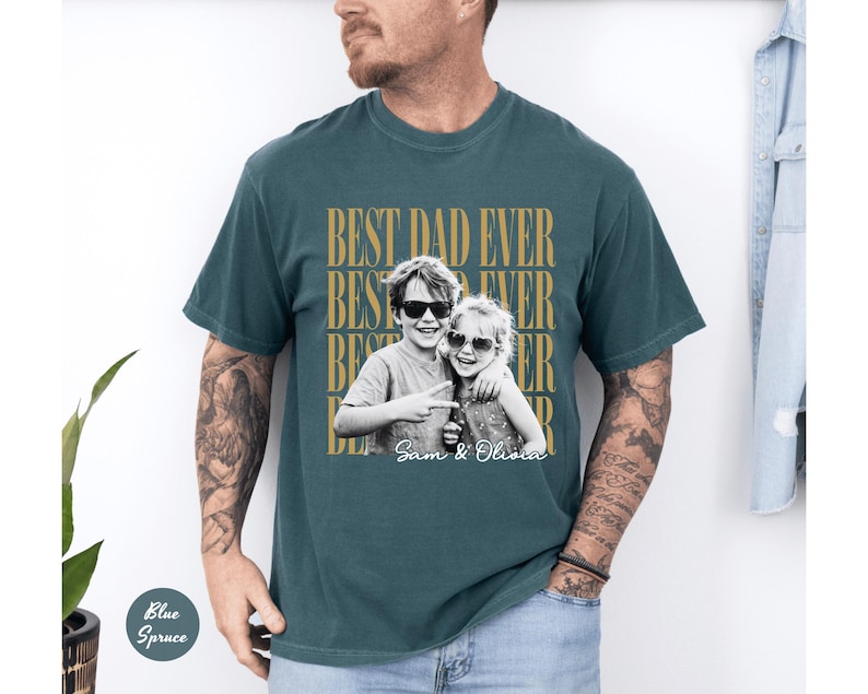 May include: Teal-colored t-shirt with the text "BEST DAD EVER" in a repeating pattern. A black and white photo of two children wearing sunglasses is centered on the shirt, with the names "Sam & Olivia" below.