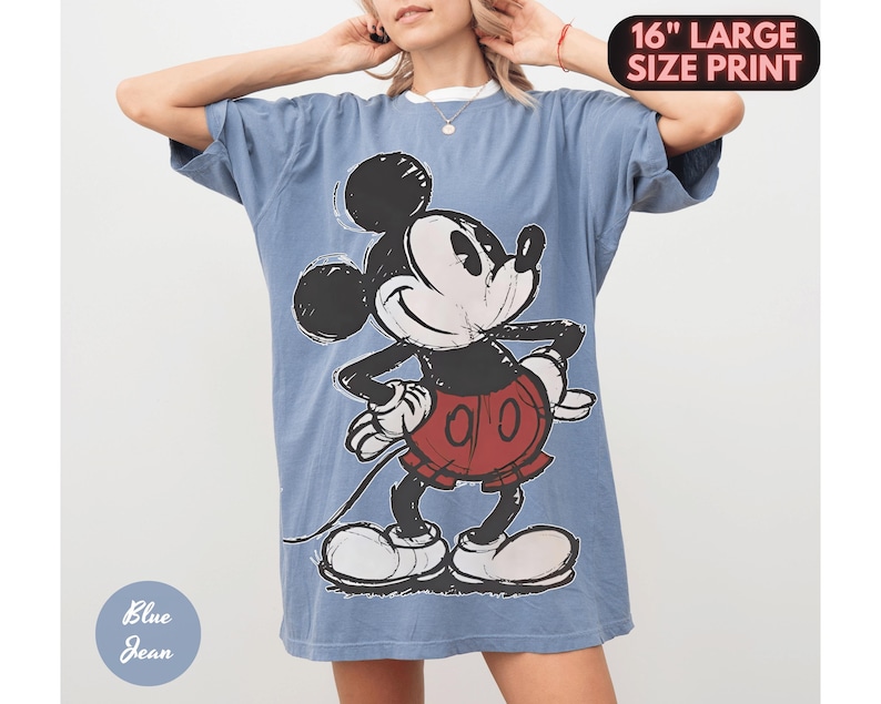 Puede incluir: Una camiseta vaquera azul con un gran gr&aacute;fico de Mickey Mouse. El personaje de dibujos animados es en negro, blanco y rojo. La camiseta tiene una impresi&oacute;n de gran tama&ntilde;o de 40,6 cm.