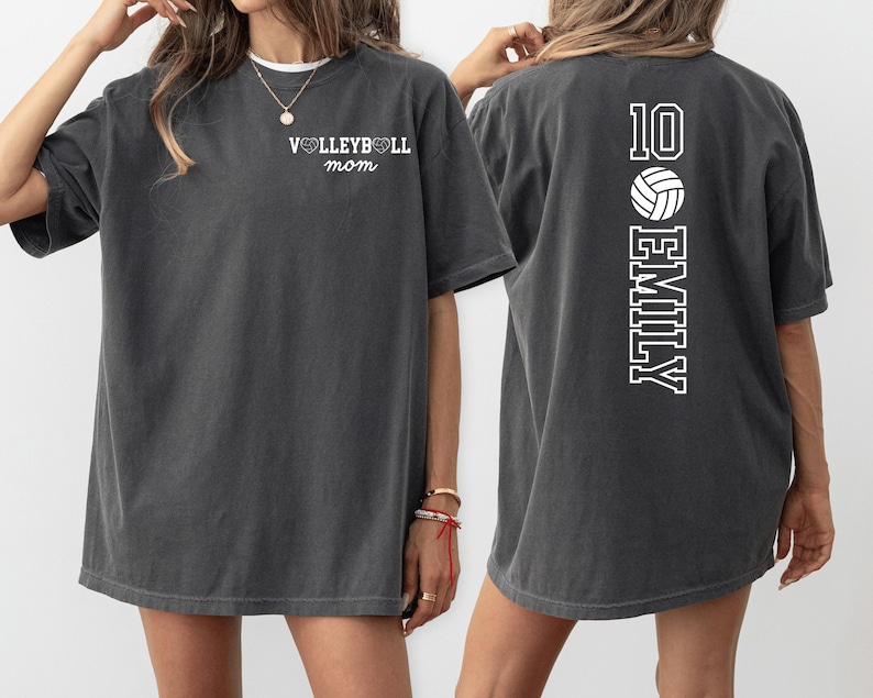 May include: Dark gray t-shirt with the text "VOLLEYBALL mom" on the front and "10 EMILY" with a volleyball graphic on the back. The shirt has a crew neck and short sleeves. The shirt is a comfortable, casual style.