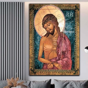 May include: A framed religious icon depicting a figure with a crown of thorns, wearing a red robe, and set against a teal background. The icon has a gold border and is displayed above a gray sofa. The artwork is a traditional religious painting.