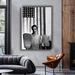 Puede incluir: Impresión en blanco y negro de una mujer sosteniendo una escoba y una fregona frente a una bandera estadounidense. La mujer lleva gafas y un vestido de lunares. La imagen es un retrato.