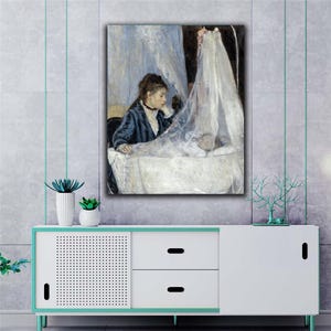 以下が含まれることがあります： 額縁に入った絵画には、濃い青色のジャケットを着た女性が揺りかごの中の赤ちゃんを見ている様子が描かれています。揺りかごは透明な白い布で覆われています。このアートワークは、白とティール色のキャビネットの上に展示されています。