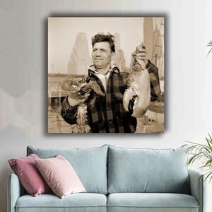 May include: Sepia-toned print of a man holding two lobsters. The man wears a plaid shirt and looks towards the upper left. The background shows a cityscape. The lobster claws are prominent.