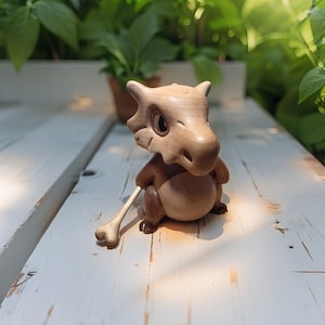 May include: A handcrafted wooden figurine of a Cubone character, featuring a light brown head and body with darker brown accents. The figure is holding a bone and is positioned on a white wooden surface.