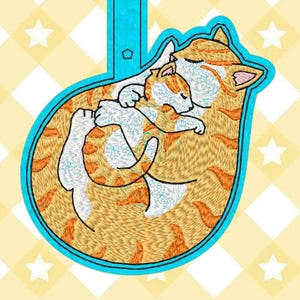 May include: Orange and white tabby cat curled up sleeping with a smaller orange and white tabby kitten. The cats are embroidered on a blue fabric with a blue loop at the top.