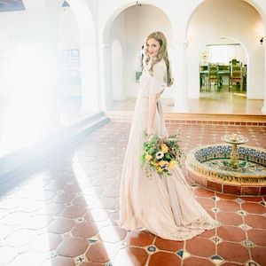 Woman with bouquet walking through Courtyard in the Coralie Beatrix exclusive Beige tulipcut with lace Infinity Wrap Multiway dress.  Honeymoon, Elopement, Anniversary, Vow Renewal, Weddings, Shower, Gift, Family Photos, etc. dress