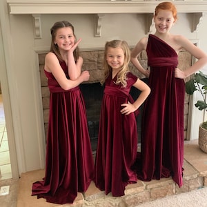 Three smiling Junior Bridesmaids in Burgundy Velvet dresses. Infinity Wrap dresses Wrapped in different ways- Grecian, one shoulder, sleeves, halter.