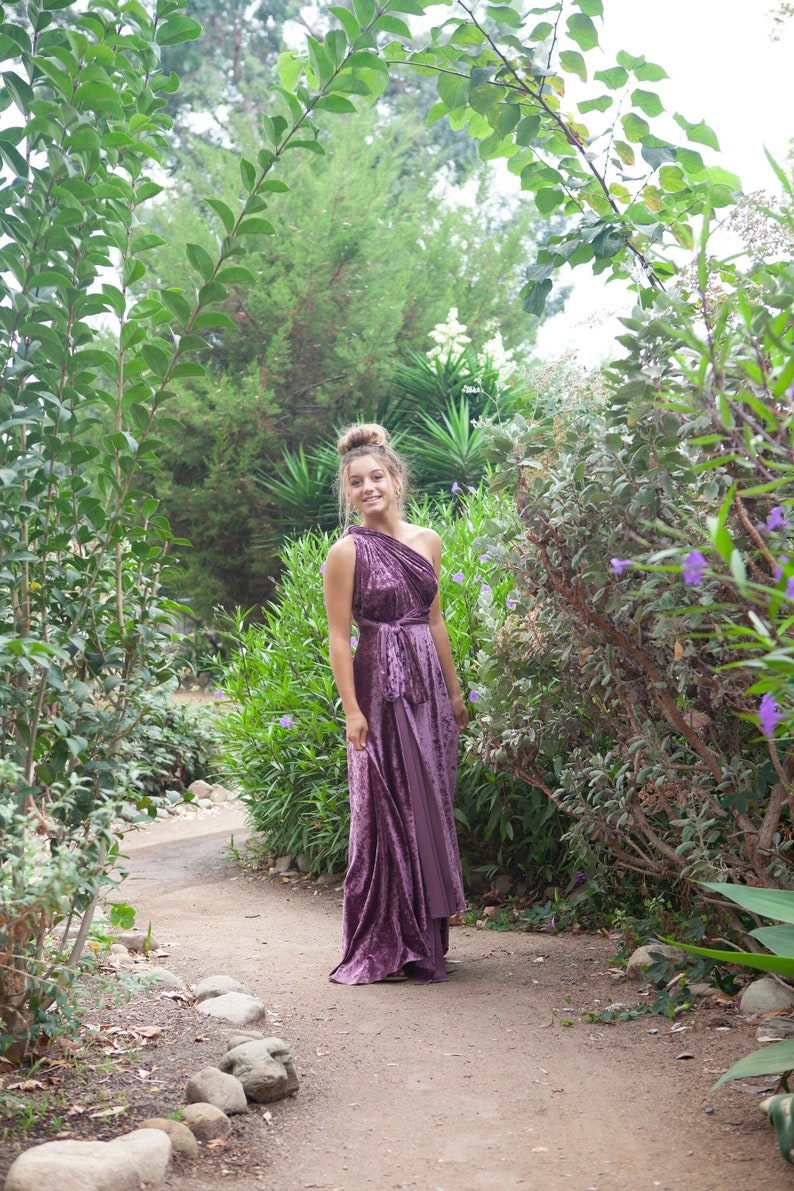 A woman wearing a one-shoulder, purple velvet maxi dress with a cinched waist and a flowing skirt.