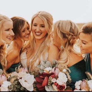 bridal party in teal green dresses with bouquets of flowers, smiling and looking at the camera.