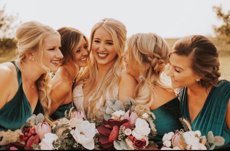 bridal party in teal green dresses with bouquets of flowers, smiling and looking at the camera.