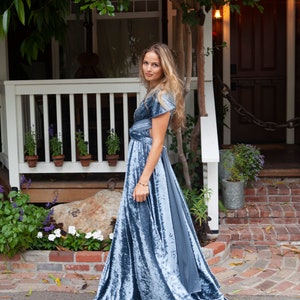 A woman wearing a blue velvet maxi dress with a flowing skirt.