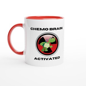 May include: White ceramic mug with a red rim. The mug features a black and white graphic of a turtle with a radiation symbol and the text "CHEMO BRAIN ACTIVATED".