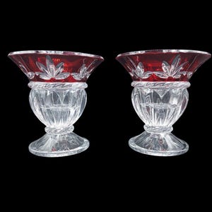 May include: A pair of clear and ruby red cut glass bowls featuring a flared rim with a floral pattern, a bulbous body with vertical facets, and a circular base. Each bowl has a twisted rope-like texture around the neck and the foot.