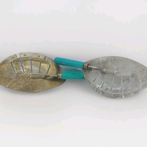 May include: Two metal scoops with bright turquoise handles. Each scoop features a semi-circular, leaf-like shape with a series of embossed lines radiating from the handle attachment point. One scoop has a weathered, golden-toned patina.