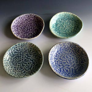May include: Four small ceramic bowls with a white floral pattern. The bowls are in shades of purple, blue, and green.
