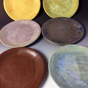May include: Six ceramic plates in various colors and patterns. The plates are round and have a smooth, glazed finish. The colors include yellow, green, purple, brown, and blue.
