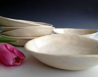 May include: A set of five white ceramic bowls with a slightly textured surface. The bowls are stacked on top of each other, with the largest bowl at the bottom and the smallest bowl at the top.