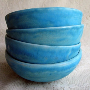 May include: Stack of four blue ceramic bowls with a crackled glaze. The bowls are nested inside each other, with the largest bowl at the bottom and the smallest bowl at the top.