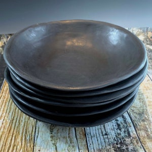 May include: A stack of five black ceramic bowls. The bowls are round and have a slightly raised rim. They are all the same size and shape.
