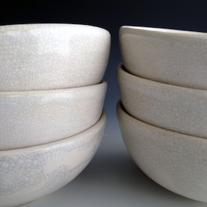 May include: A stack of five white ceramic bowls with a crackled glaze finish. The bowls are nested together, with the largest bowl at the bottom and the smallest bowl at the top.