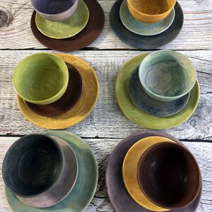 May include: Set of six ceramic bowls and plates in various shades of green, blue, yellow, and brown. The bowls and plates are stacked on top of each other.
