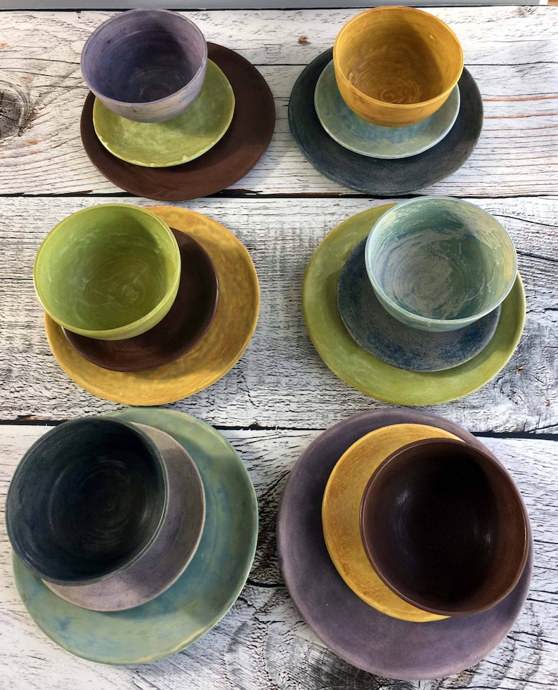 May include: Set of six ceramic bowls and plates in various shades of green, blue, yellow, and brown. The bowls and plates are stacked on top of each other.