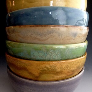 May include: A stack of six ceramic bowls in various shades of brown, yellow, green, and blue. The bowls are nested together, with the largest bowl at the bottom and the smallest bowl at the top.