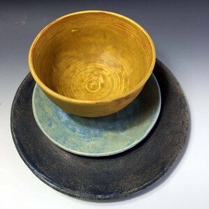 May include: A set of three ceramic dishes in a yellow, blue, and dark gray color scheme. The dishes are stacked on top of each other, with the yellow bowl on top.