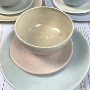 Puede incluir: Un juego de vajilla de cer&aacute;mica en colores pastel. El juego incluye cuencos, platillos y platos en tonos azul claro, rosa y beige. Los cuencos est&aacute;n colocados encima de los platos y platillos, creando un efecto de capas. La cer&aacute;mica tiene un esmalte craquelado.
