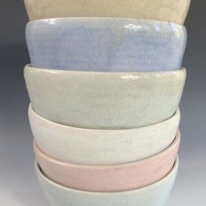 Puede incluir: Una pila de seis cuencos de cer&aacute;mica en colores pastel. Los cuencos est&aacute;n apilados uno encima del otro, con el cuenco superior de color beige claro. Los otros cuencos son azul claro, verde, blanco, rosa y azul claro en la parte inferior.