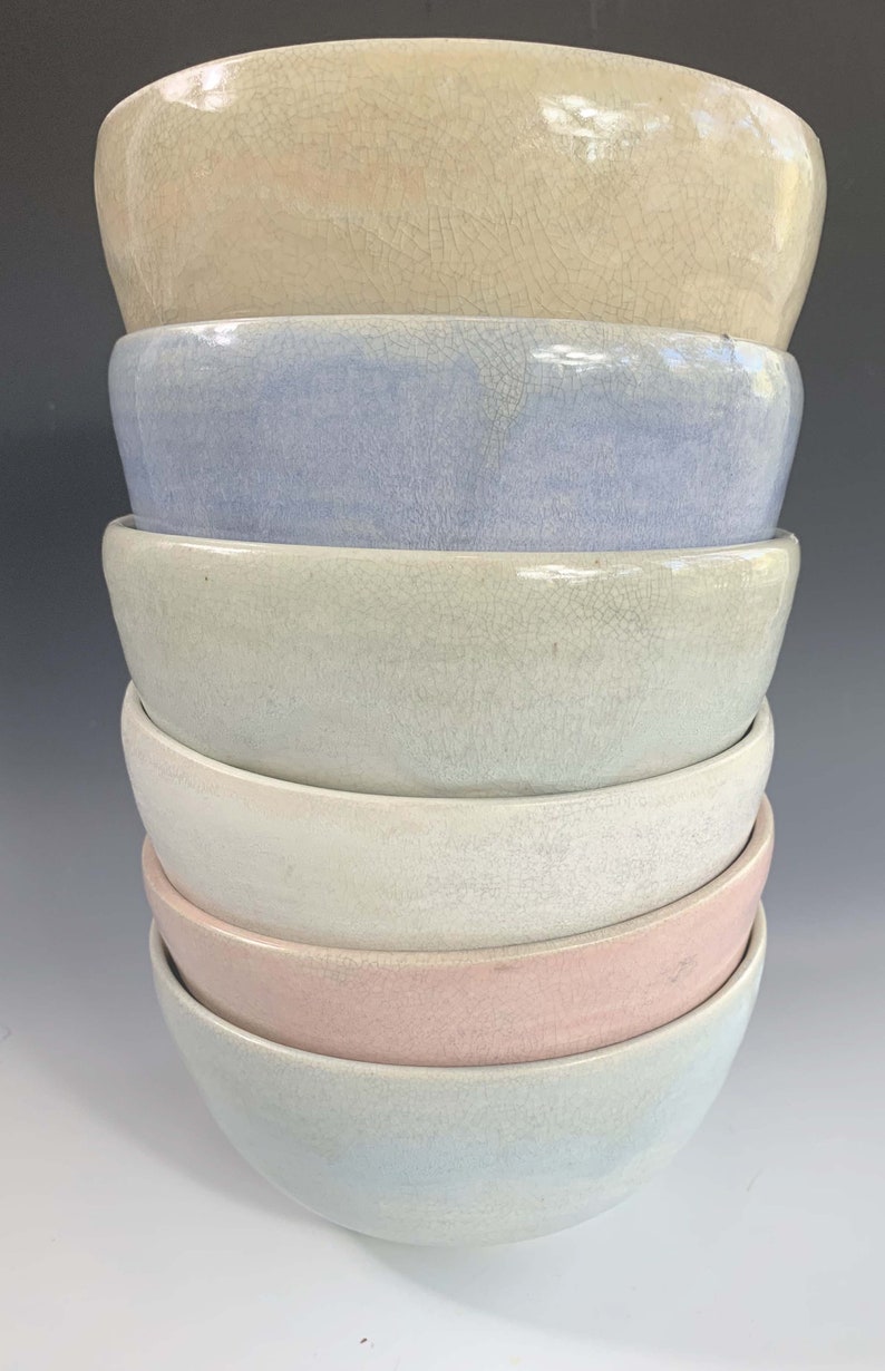 Puede incluir: Una pila de seis cuencos de cer&aacute;mica en colores pastel. Los cuencos est&aacute;n apilados uno encima del otro, con el cuenco superior de color beige claro. Los otros cuencos son azul claro, verde, blanco, rosa y azul claro en la parte inferior.