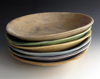 May include: A stack of five ceramic bowls in various shades of brown, green, yellow, and blue. The bowls are all slightly different sizes and shapes, and they are stacked on top of each other.