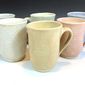 May include: Six ceramic mugs in various pastel colors, including light blue, light green, beige, and pink. The mugs have a textured, crackled glaze and are all the same size and shape.