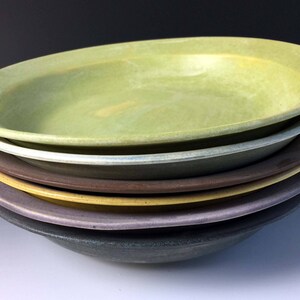 May include: A stack of six ceramic bowls in various shades of green, brown, yellow, purple, and gray. The bowls are nested together, with the largest bowl on top.