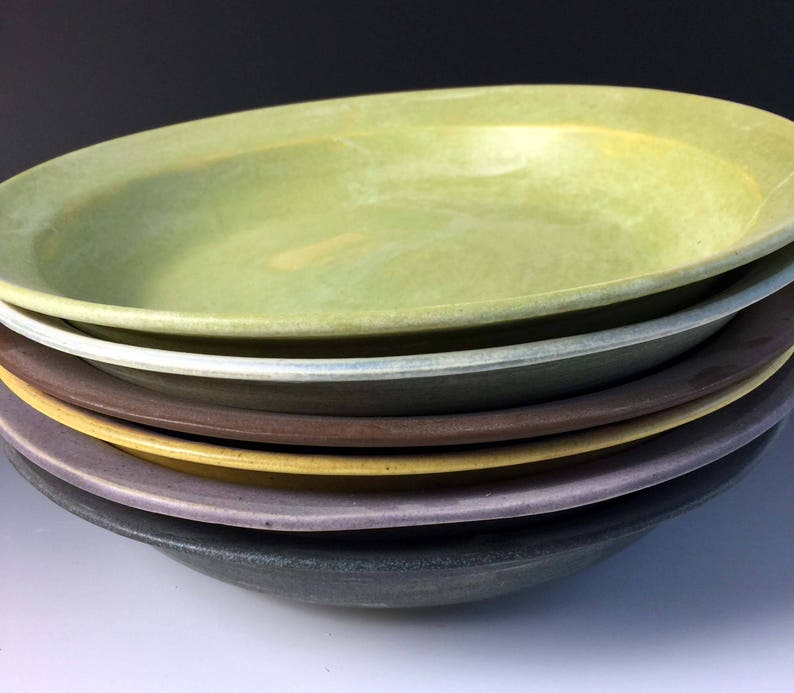 May include: A stack of six ceramic bowls in various shades of green, brown, yellow, purple, and gray. The bowls are nested together, with the largest bowl on top.