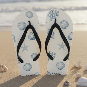 Op de afbeelding: Een paar witte slippers met een blauw patroon van diverse schelpen, zeesterren en koraal. Het schoeisel heeft zwarte rubberen teenslippers en de tekst FLYLIVING in kleine zwarte letters gedrukt bij het hielgedeelte van elke zool.