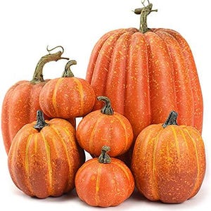 May include: A collection of seven artificial pumpkins in varying sizes, featuring a textured orange surface with yellow speckles and prominent vertical ridges. Each pumpkin is topped with a dark brown, curved stem, arranged in a cluster.