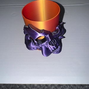 May include: A 3D printed orange and yellow cup with a purple skull design.