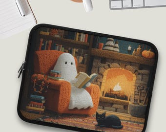 Puede incluir: Funda negra para portátil con una escena acogedora: un fantasma leyendo en un sillón naranja junto a una chimenea. Un gato negro está sentado en la alfombra. El fondo incluye una estantería y un árbol de Navidad.