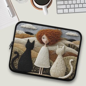 Puede incluir: Una funda negra para portátil con un diseño caprichoso. Representa una muñeca pelirroja, un gato negro y un gato blanco, sobre un paisaje de colinas y nubes. La funda tiene una cremallera negra.
