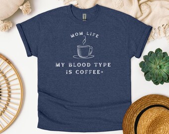 May include: A navy blue t-shirt with white text that reads "Mom Life My Blood Type Is Coffee+". The shirt features a simple illustration of a coffee cup with steam rising from it.