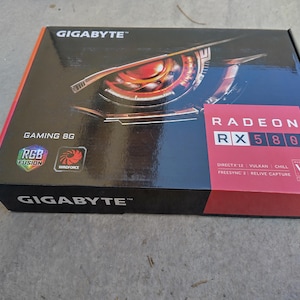 Könnte beinhalten: Schwarze und rote Gigabyte Radeon RX 580 Gaming 8G Grafikkarte-Box. Die Box zeigt das Gigabyte-Logo, den Namen Radeon RX 580 und die Logos RGB Fusion und Windforce. Die Box liegt auf einer grauen Oberfläche.
