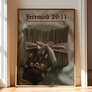 May include: Framed art print featuring a hand adorned with gold rings and long, embellished nails. The artwork includes a bundle tied with a pink ribbon and the text "Jeremiah 29:11" with a quote. The color palette includes gold, brown, and pink.