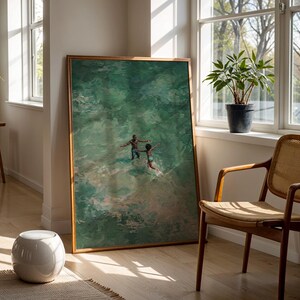 May include: A framed art print depicts two figures in turquoise water, arms outstretched. The artwork is displayed in a well-lit room with a wooden chair, a potted plant, and a white ceramic stool. The frame is a warm, natural wood tone.